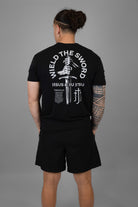 Person wearing a black t-shirt with white text and WIELD THE SWORD graphic on the back, standing against a gray background.