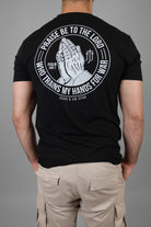man wearing black tee with praying hands graphic on back with text "PRAISE BE TO THE LORD WHO TRAINS MY HANDS FOR WAR"