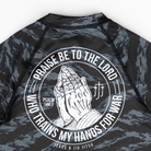 Black and gray camouflage rash guard with praying hands graphic and text on a white background